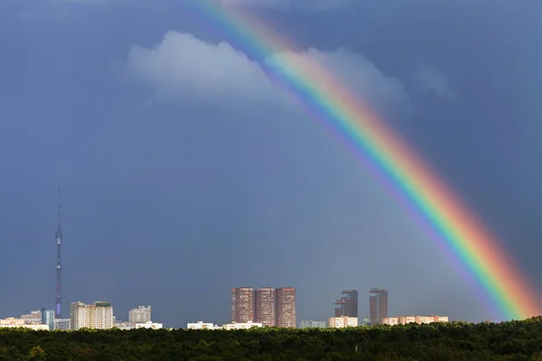 Regnbue i mørkeblå himmel over byen med TV-tårn – stockfoto