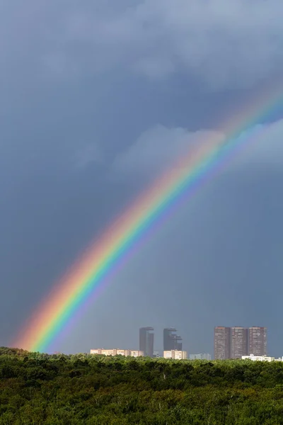 Arco iris en la lluvia sobre la ciudad y árboles verdes —  Fotos de Stock