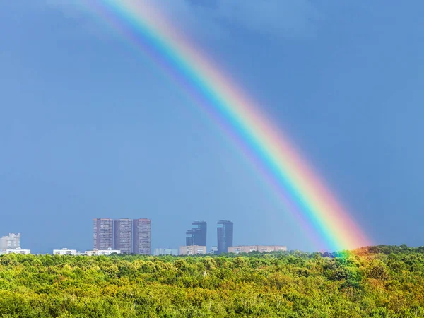 Regenboog in blauwe regenachtige hemel over stad en stedelijk park — Stockfoto