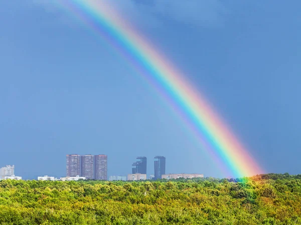 Arcobaleno nel cielo blu piovoso sopra la città e il parco urbano — Foto Stock