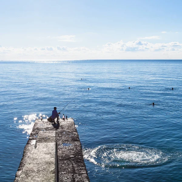 Pescatore sul molo e turisti nuoto nel Mar Nero — Foto Stock