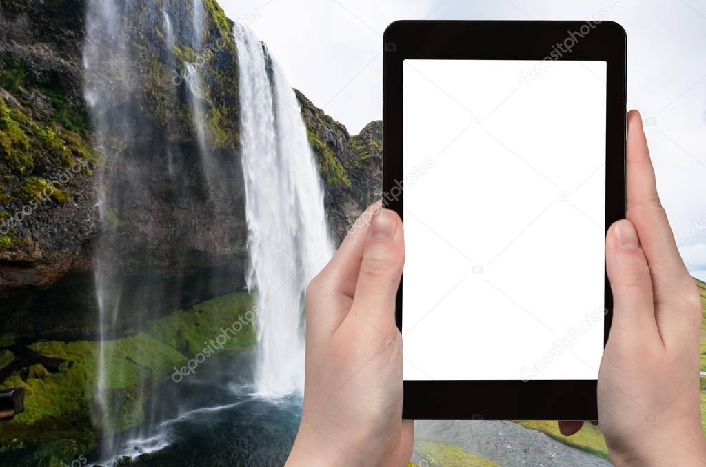 Travel concept - tourist photographs Seljalandsfoss waterfall of Seljalands River in Katla Geopark in Iceland in autumn on tablet with cut out screen for advertising logo