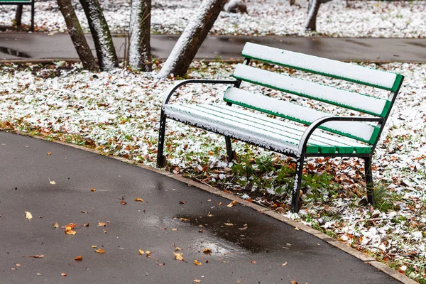 První sníh na dřevěné lavičce v městském parku — Stock fotografie