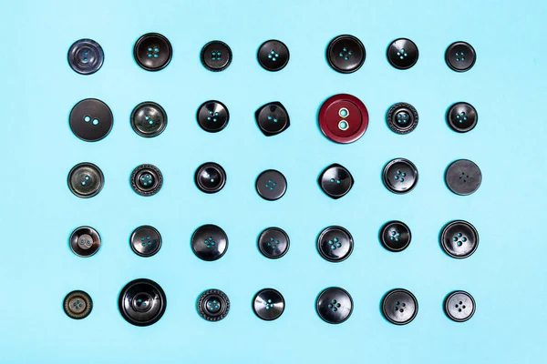 Bouton rouge entre de nombreux boutons noirs sur bleu — Photo