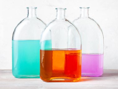 Gri beton duvarın yanında gri tahta üzerinde suluboya çözeltileri olan cam mataralar.