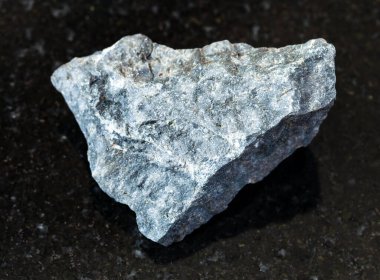 Jeolojik koleksiyondaki doğal mineral örneğinin yakın çekimi - Siyah granit arka plandaki kaba gri bazalt kaya