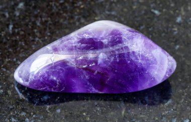 Jeolojik koleksiyondaki doğal mineral örneğinin yakın çekimi - Namibya 'dan siyah granit arka planda yuvarlanan Ametist kayası