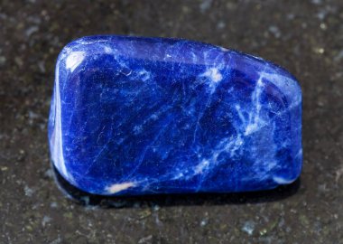 Jeolojik koleksiyondaki doğal mineral örneğinin yakın çekimi - Brezilya 'dan siyah granit arka planda yuvarlanan Sodalite kayası