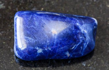 Jeolojik koleksiyondaki doğal mineral örneğinin yakın plan fotoğrafı. Brezilya 'dan siyah granit zemin üzerine yuvarlanmış Sodalite kayası.
