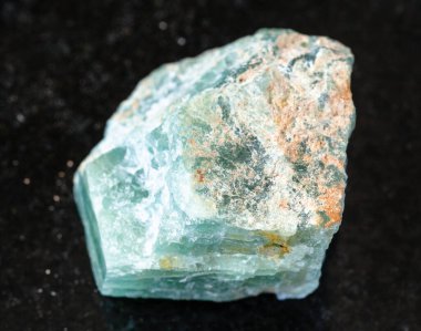 Jeolojik koleksiyondaki doğal mineral numunesinin yakın çekimi. Siyah granit arka plandaki ham Apatite kayası.