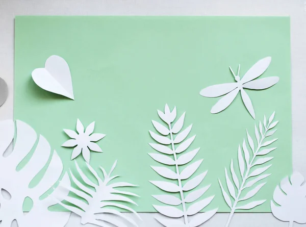 white paper leaves on the green background, white paper dragonfly on the green background, white paper heart on the green background