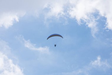 Mavi gökyüzünde bulutlarla süzülen paraglider
