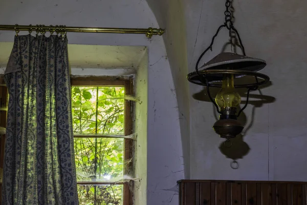 Terk edilmiş bir handa perdesi olan bir pencerenin yanında lamba.