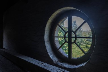 Terk edilmiş bir manastırın karanlık tavan arasında yuvarlak bir pencere.