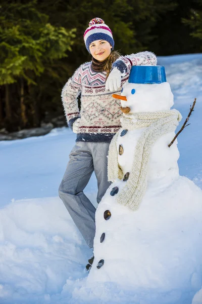 Щаслива усміхнена дівчина-підліток грає зі сніговиком на сніжній перемозі — стокове фото