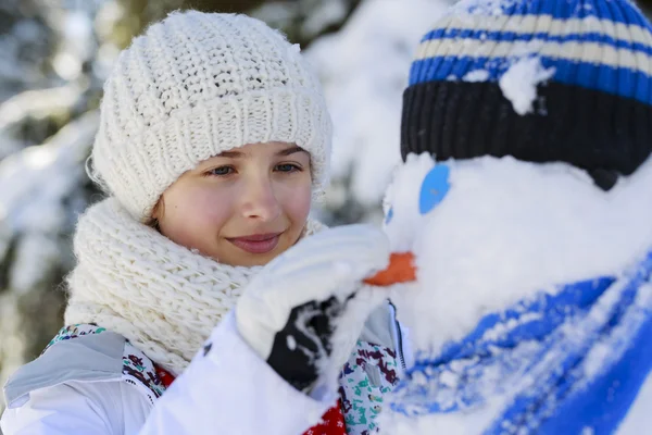 Счастливая улыбающаяся девочка-подросток, играющая со снеговиком в снежной победе — стоковое фото