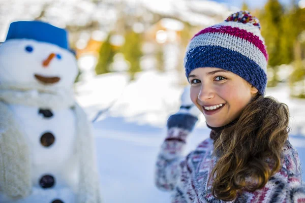 Happy smiling teenage girl playing with a snowman on a snowy win — Stock Photo, Image