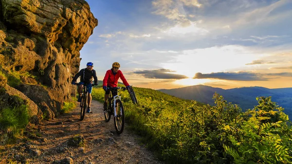 Mountain biking women and man riding on bikes at sunset mountain — Stock Photo, Image