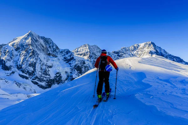 Esquí de montaña caminando a lo largo de una cresta nevada con esquís en el bac —  Fotos de Stock