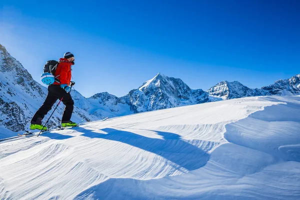 Esquí de montaña caminando a lo largo de una cresta nevada con esquís en el bac —  Fotos de Stock
