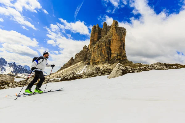 登山家野外滑雪春天走在白雪皑皑的山脊与滑雪板在背包里。在蓝色背景多云的天空和阳光在南蒂罗尔，白云岩，意大利蒙特优雅。冒险冬季极限运动. 免版税图库图片
