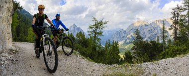 Tourist cycling in Cortina d'Ampezzo, stunning rocky mountains o clipart