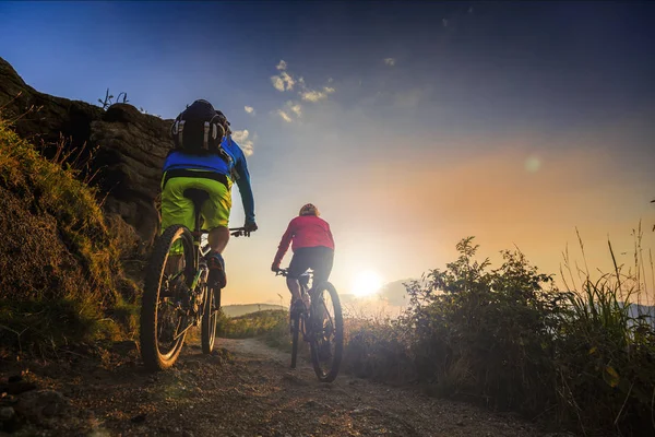 山地自行车的妇女和男子骑着自行车在日落山 — 图库照片