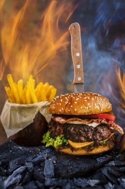 Lezzetli füme ızgara ve sırlı sığır eti burger marul, peynir ve domuz pastırması arka planda boşaltmak, duman ve ateş ahşap Ahşap tablo patates kızartması ile servis.