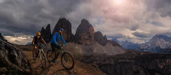 Cycling outdoor adventure in Dolomites. Cycling woman and man  on electric mountain bikes in Dolomites landscape. Couple cycling MTB enduro trail track. Outdoor sport activity.