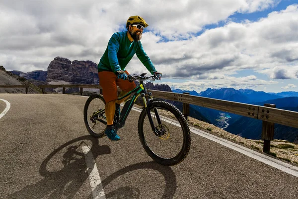 Man cycling on electric bike, rides mountain trail. Man riding on bike in Dolomites mountains landscape. Cycling e-mtb enduro trail track. Outdoor sport activity.