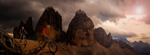 Cycling outdoor adventure in Dolomites. Cycling woman and man  on electric mountain bikes in Dolomites landscape. Couple cycling MTB enduro trail track. Outdoor sport activity.