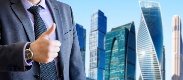 Portrait of businessman shows thumbs up gesture over cityscape background. — Stock Photo, Image