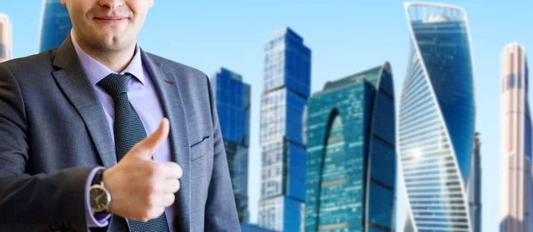 Portrait of businessman shows thumbs up gesture over cityscape background. — Stock Photo, Image