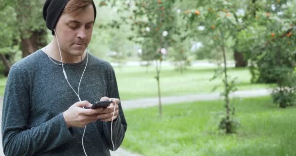Hipster listening to music from smartphone in the summer park. — Stock Video