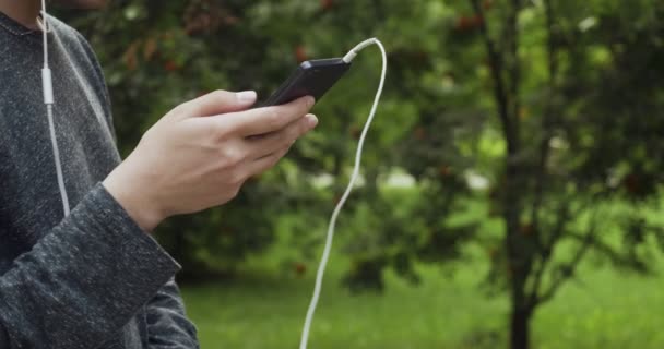 Young man types on smartphone with headphhones. — Stockvideo