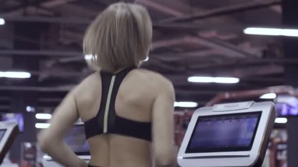 在体育馆的跑步机上跑步的年轻的女运动员. — 图库视频影像