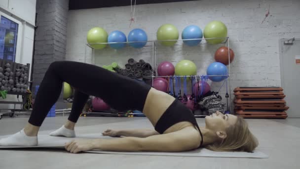 Женщина делает упражнения на коврике на различных инвентарных фоне . — стоковое видео