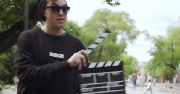 Young man with clapperboard appears and leaves the frame. — Stockvideo