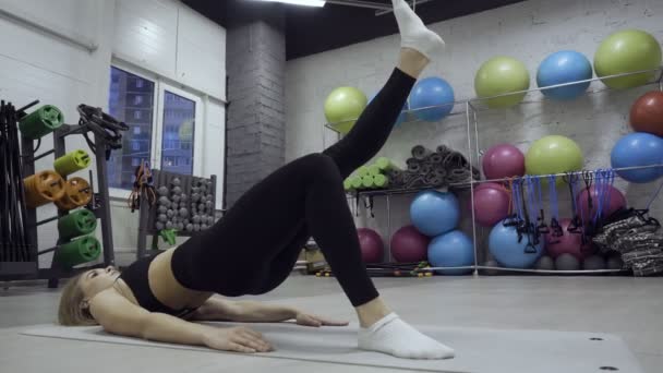 Женщина делает упражнения на коврике на различных инвентарных фоне . — стоковое видео
