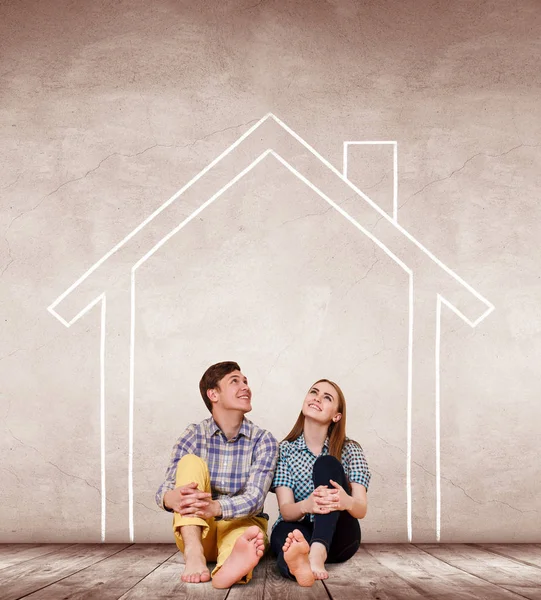 Casal feliz sentado no chão dentro da casa pintada na parede . — Fotografia de Stock