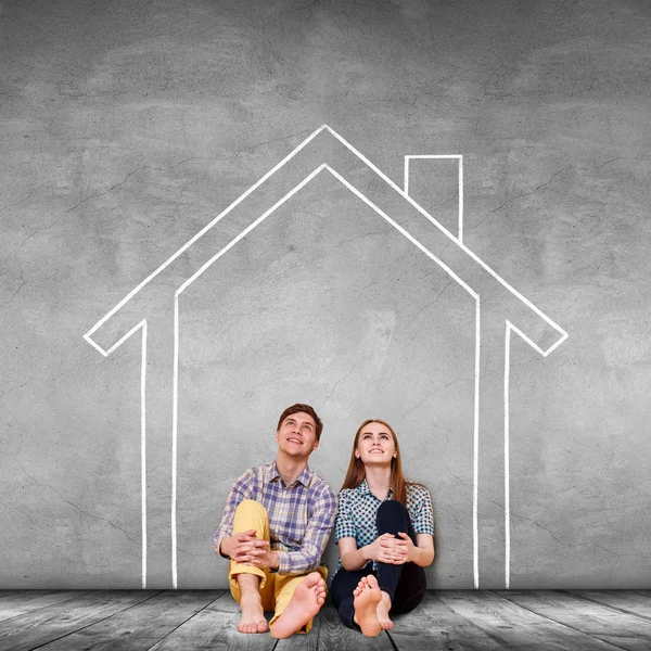 Happy couple sitting on the floor inside painted house on the wall. — Stock Photo, Image