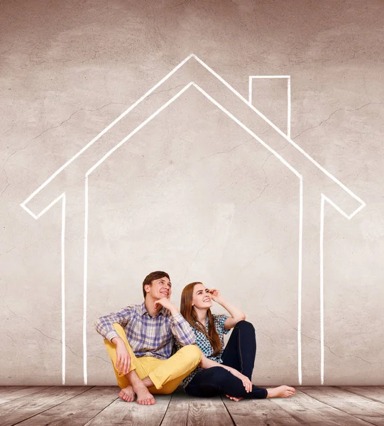 Happy couple sitting on the floor inside painted house on the wall. — Stock Photo, Image