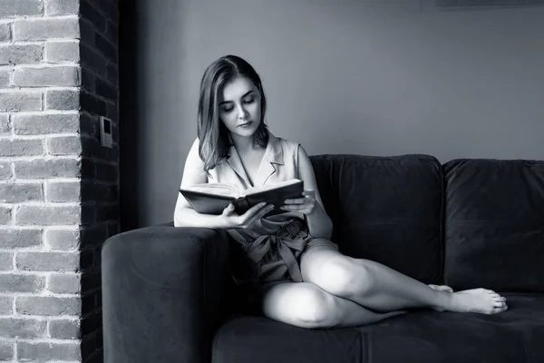 Mujer joven se sienta y relajarse en el sofá y mira en su diario . —  Fotos de Stock