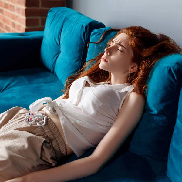 Young redhead woman reclining on the couch and feels tired. — Stock Photo, Image