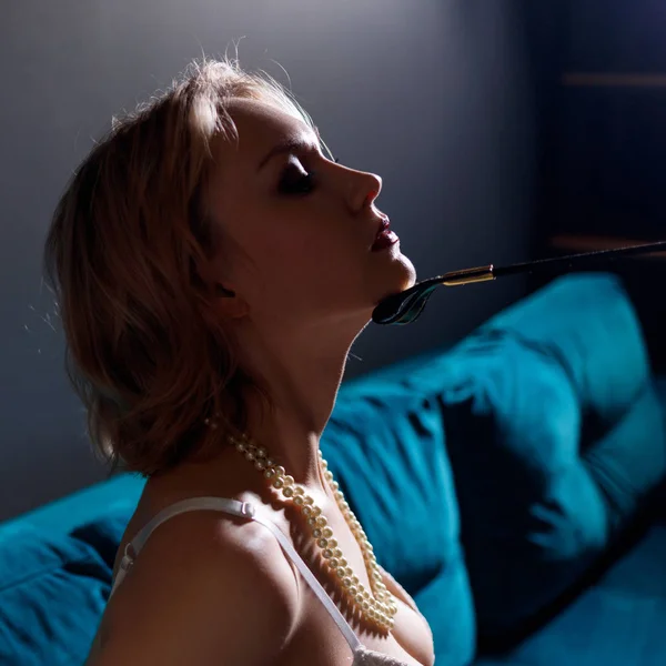Blonde submissive woman with leather whip touches her chin.