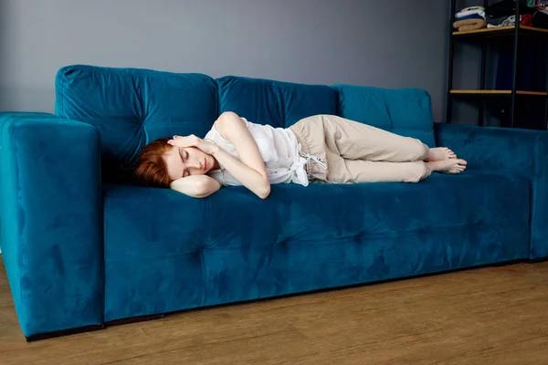 Νεαρή γυναίκα ξαπλωμένη στον καναπέ και με πονοκέφαλο στο σπίτι. — Φωτογραφία Αρχείου