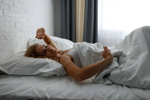 Jovem mulher despertando e alongamento em confortável cama acolhedora . — Fotografia de Stock