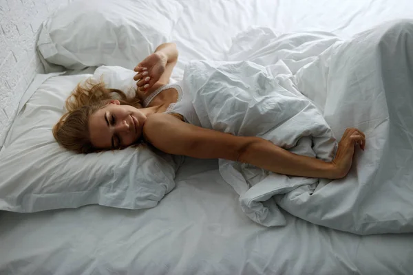 Junge Frau wacht auf und dehnt sich im bequemen, gemütlichen Bett. — Stockfoto