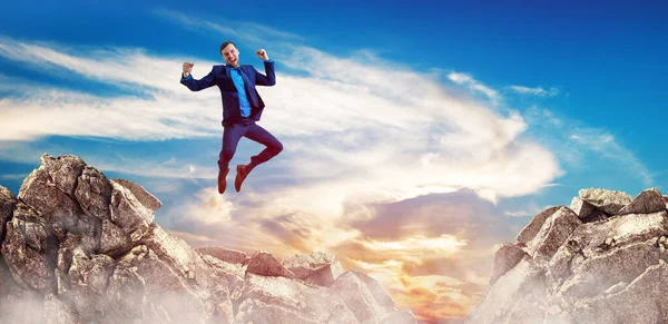 Young businessman feels success and jumps up over mountains — Stock Photo, Image