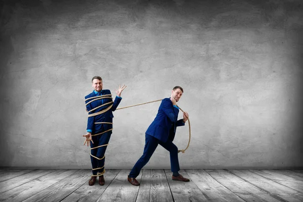 Hombre de negocios cansado tira de sí mismo atado con una cuerda . — Foto de Stock